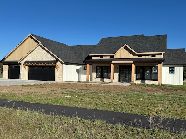 view of front of property featuring an attached garage, board and batten siding, driveway, covered porch, and a front yard