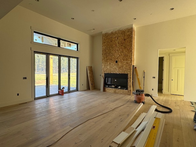 unfurnished living room with a multi sided fireplace, light wood-type flooring, a high ceiling, and baseboards