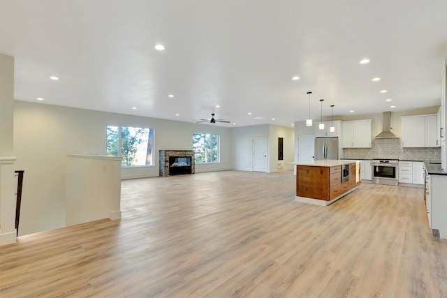 kitchen with a center island, hanging light fixtures, white cabinets, stainless steel appliances, and wall chimney range hood