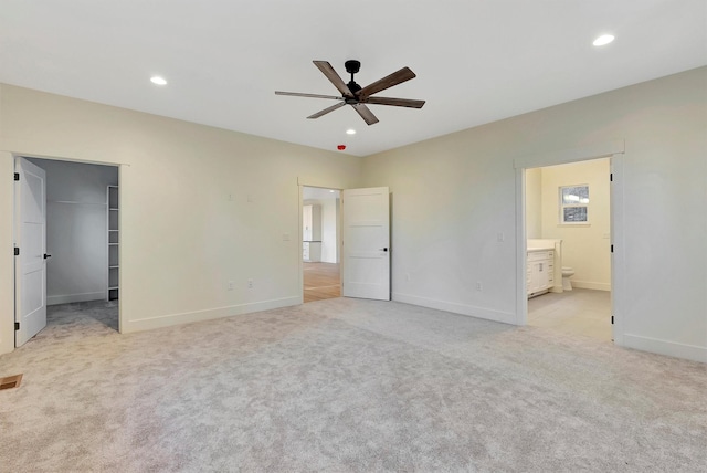 unfurnished bedroom featuring connected bathroom, a spacious closet, light carpet, and ceiling fan