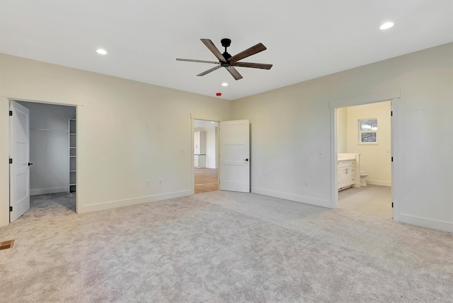 unfurnished bedroom with ensuite bathroom, ceiling fan, a spacious closet, and light carpet