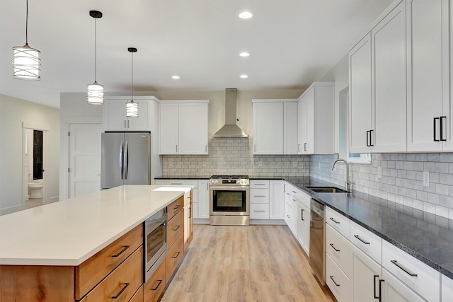 kitchen with appliances with stainless steel finishes, sink, wall chimney range hood, and white cabinets