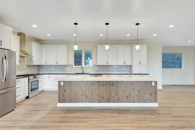 kitchen featuring a kitchen island, appliances with stainless steel finishes, decorative light fixtures, white cabinetry, and wall chimney exhaust hood