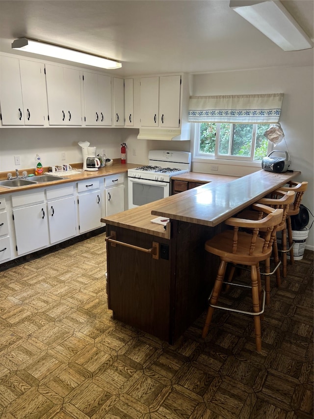 kitchen with white range with gas stovetop, a kitchen breakfast bar, kitchen peninsula, and white cabinets