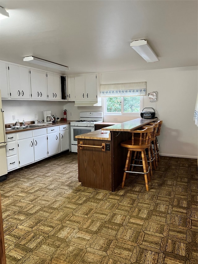 kitchen with a breakfast bar area, sink, white appliances, and white cabinetry