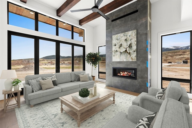 living room with beamed ceiling, a tile fireplace, light hardwood / wood-style flooring, ceiling fan, and a towering ceiling