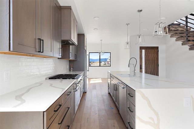 kitchen featuring light wood-type flooring, pendant lighting, light stone counters, sink, and a large island