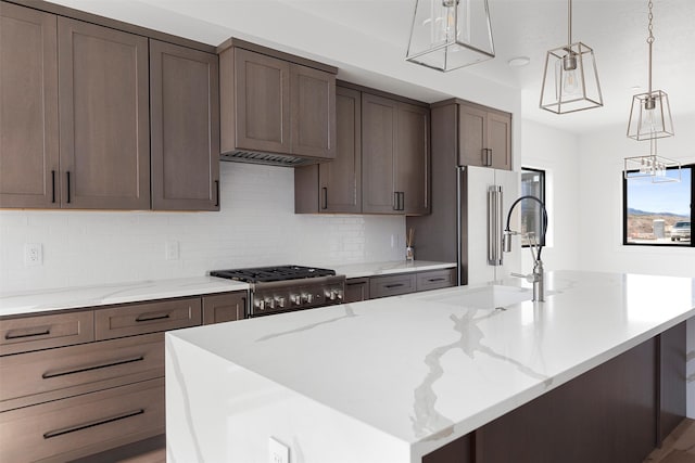 kitchen with light stone counters, a center island with sink, and hanging light fixtures