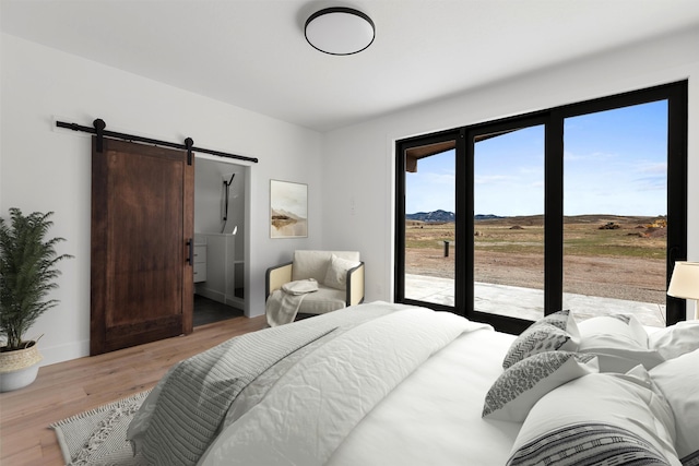 bedroom with a barn door, light wood-type flooring, and access to exterior