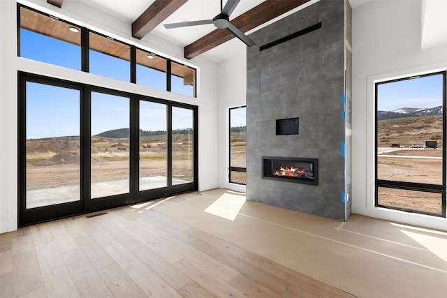 unfurnished living room featuring light hardwood / wood-style flooring, a large fireplace, beamed ceiling, a high ceiling, and ceiling fan