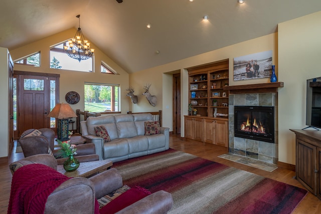 living room featuring high vaulted ceiling, a chandelier, a tile fireplace, and light hardwood / wood-style floors