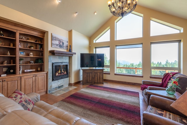 living room featuring a tiled fireplace, high vaulted ceiling, a notable chandelier, and light hardwood / wood-style floors