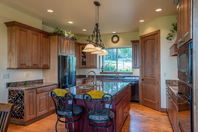 kitchen featuring black appliances, sink, light wood-type flooring, and a kitchen island with sink