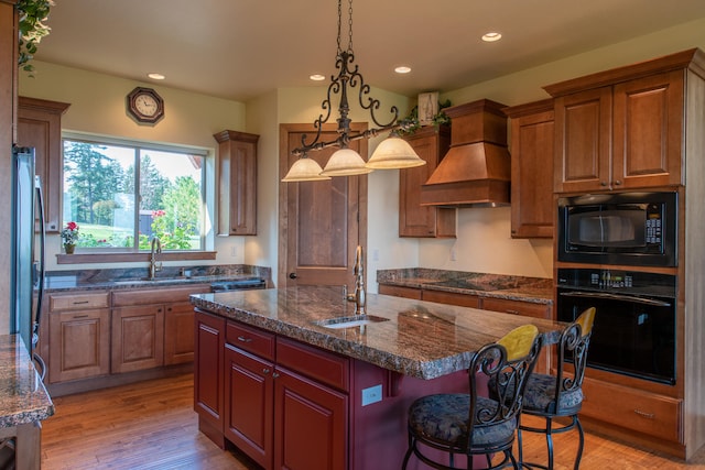 kitchen with black appliances, premium range hood, light hardwood / wood-style floors, a center island, and sink