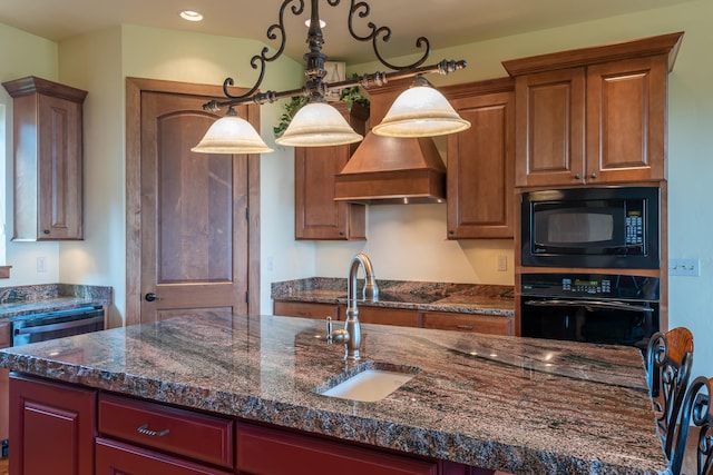 kitchen featuring decorative light fixtures, black appliances, an island with sink, sink, and dark stone counters