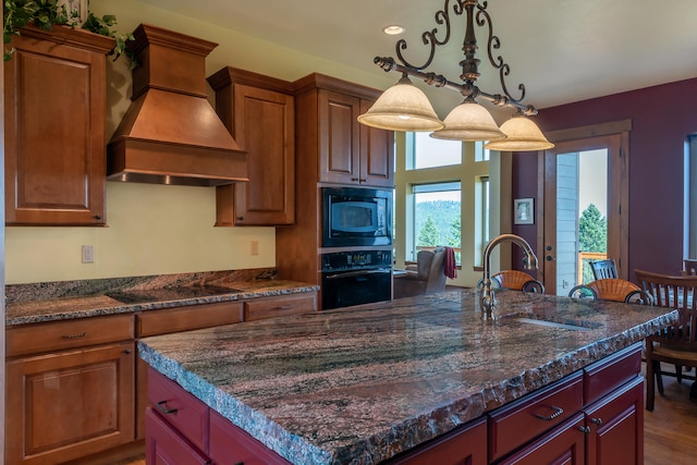 kitchen with a chandelier, black appliances, sink, custom range hood, and a center island with sink