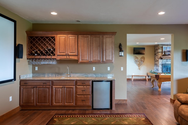 bar featuring stainless steel refrigerator, pool table, sink, dark hardwood / wood-style floors, and a stone fireplace