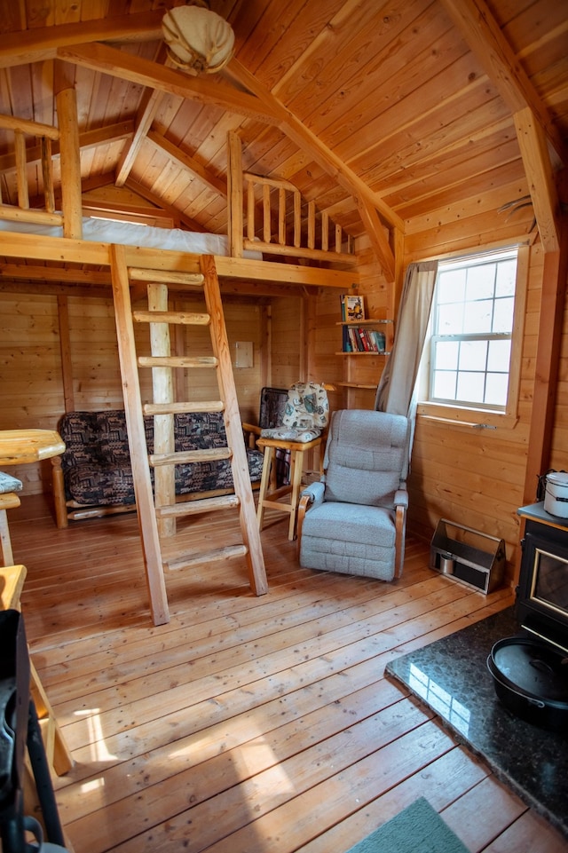 living area featuring wooden walls, wood ceiling, a wood stove, wood-type flooring, and lofted ceiling with beams