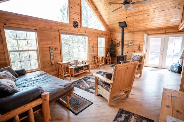 living room featuring wood walls, a wood stove, light hardwood / wood-style floors, high vaulted ceiling, and ceiling fan