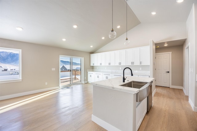 kitchen featuring light stone counters, decorative light fixtures, an island with sink, light wood-type flooring, and white cabinets