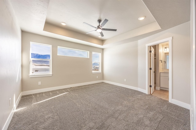 carpeted empty room with a raised ceiling and ceiling fan