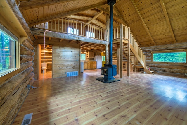 unfurnished living room featuring a wood stove, plenty of natural light, wood-type flooring, and high vaulted ceiling