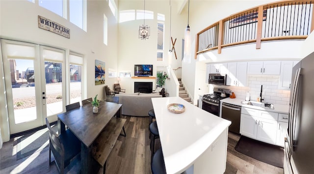 kitchen with white cabinets, stainless steel appliances, wood-type flooring, pendant lighting, and a towering ceiling