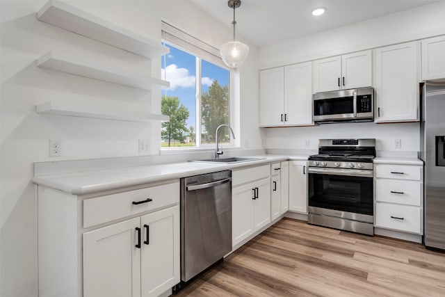 kitchen with light wood-type flooring, stainless steel appliances, white cabinetry, sink, and pendant lighting