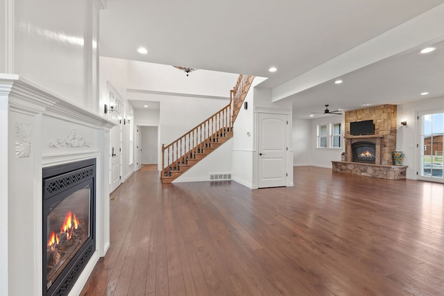 unfurnished living room featuring dark hardwood / wood-style flooring, ceiling fan, and a stone fireplace