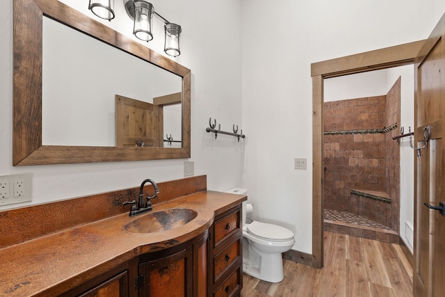 bathroom featuring vanity, a tile shower, toilet, and hardwood / wood-style flooring