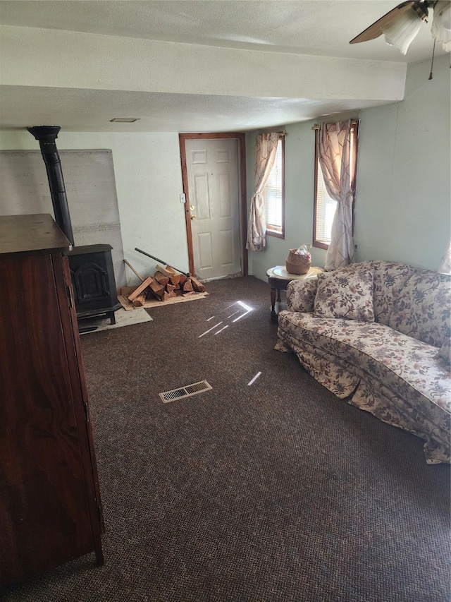 carpeted living room with a wood stove and ceiling fan