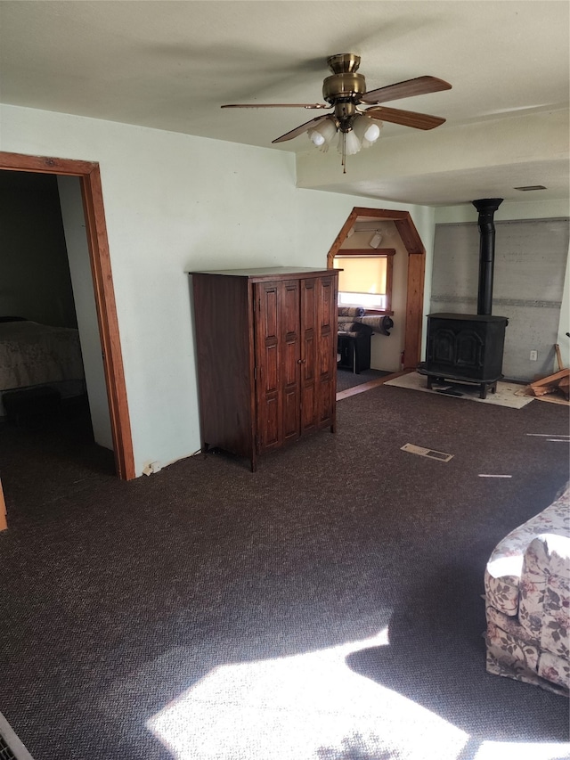 carpeted living room with a wood stove and ceiling fan