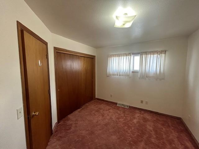 unfurnished bedroom featuring a textured ceiling, dark colored carpet, and a closet