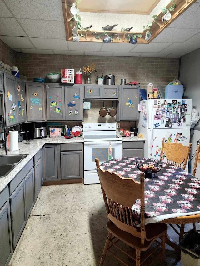 kitchen featuring white appliances, brick wall, sink, and a paneled ceiling