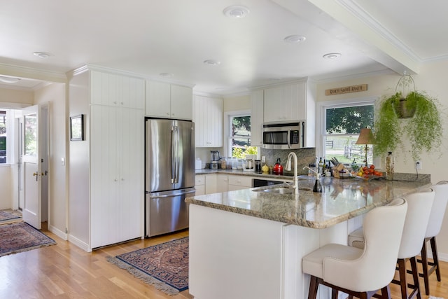 kitchen with appliances with stainless steel finishes, kitchen peninsula, white cabinetry, and light hardwood / wood-style flooring