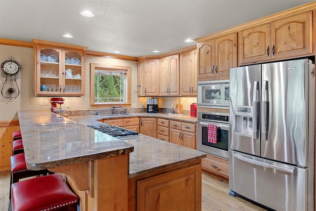 kitchen featuring stone countertops, a breakfast bar, kitchen peninsula, stainless steel appliances, and light hardwood / wood-style flooring