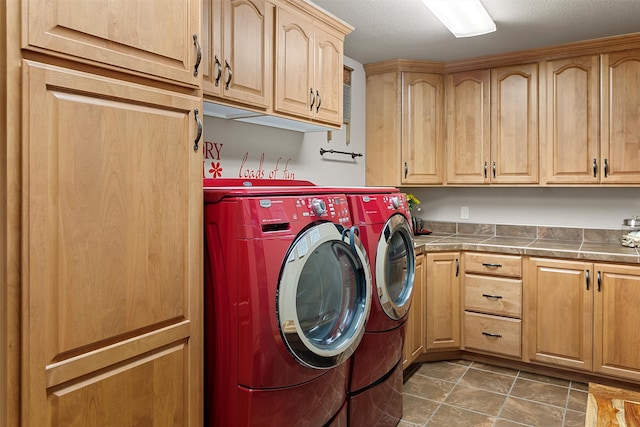 clothes washing area with dark tile patterned flooring, washing machine and dryer, and cabinets