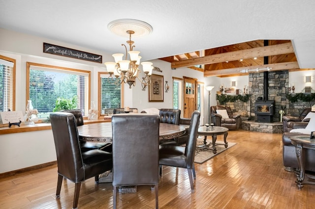 dining room with light hardwood / wood-style floors, beamed ceiling, a textured ceiling, a notable chandelier, and a wood stove