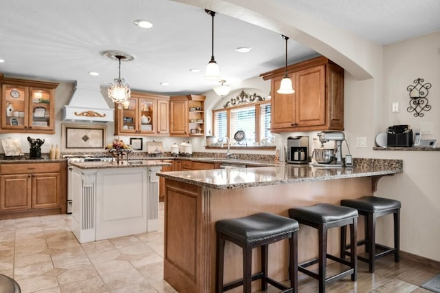 kitchen with stove, premium range hood, hanging light fixtures, kitchen peninsula, and dark stone counters