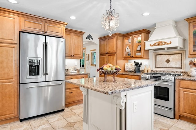 kitchen featuring light stone counters, a chandelier, a center island, custom range hood, and appliances with stainless steel finishes