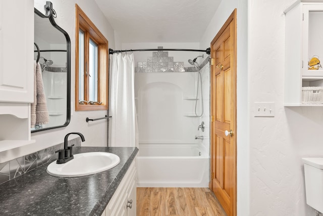 full bathroom with a textured ceiling, hardwood / wood-style floors, shower / tub combo with curtain, vanity, and toilet