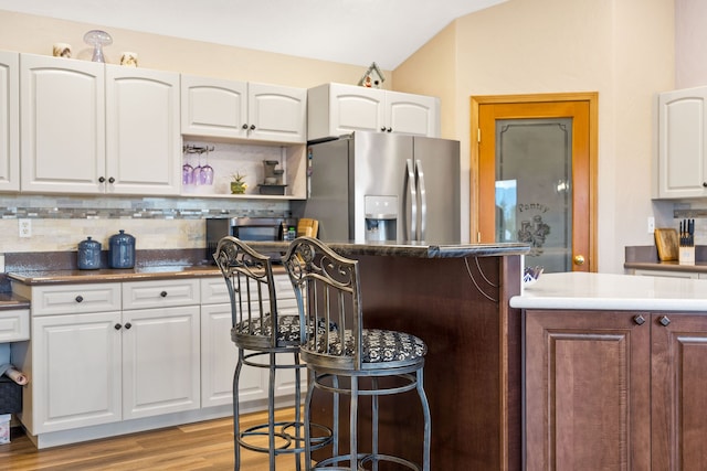 kitchen featuring light hardwood / wood-style floors, stainless steel refrigerator with ice dispenser, vaulted ceiling, white cabinetry, and decorative backsplash