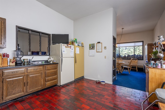 kitchen featuring brick floor, baseboards, freestanding refrigerator, brown cabinets, and dark countertops