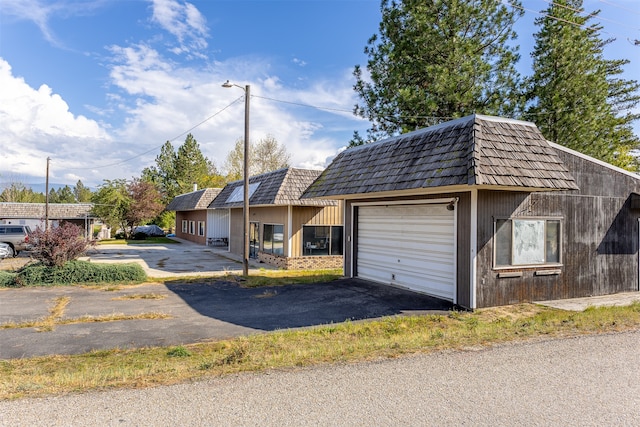 view of front of house featuring an outbuilding, brick siding, mansard roof, an attached garage, and driveway