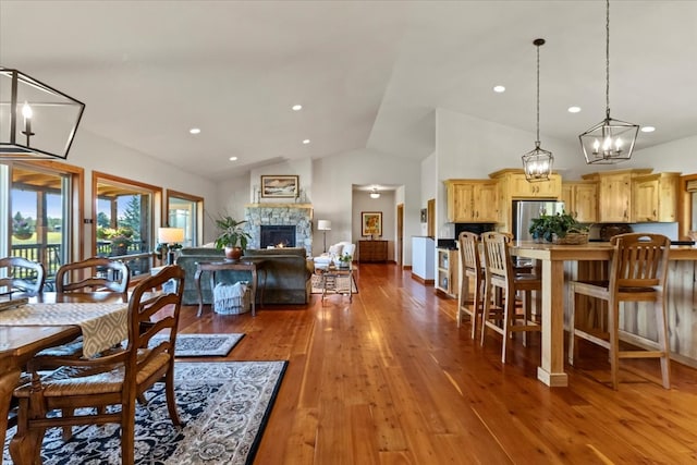 dining space featuring hardwood / wood-style flooring, a stone fireplace, and high vaulted ceiling