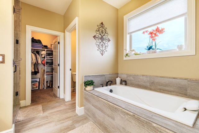 bathroom with hardwood / wood-style floors, tiled tub, and toilet