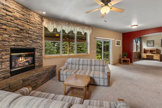 carpeted living room with ceiling fan and a stone fireplace