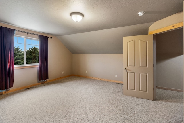 additional living space featuring a textured ceiling, lofted ceiling, and carpet flooring