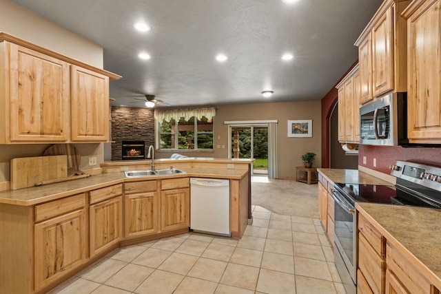 kitchen with ceiling fan, sink, kitchen peninsula, a stone fireplace, and appliances with stainless steel finishes