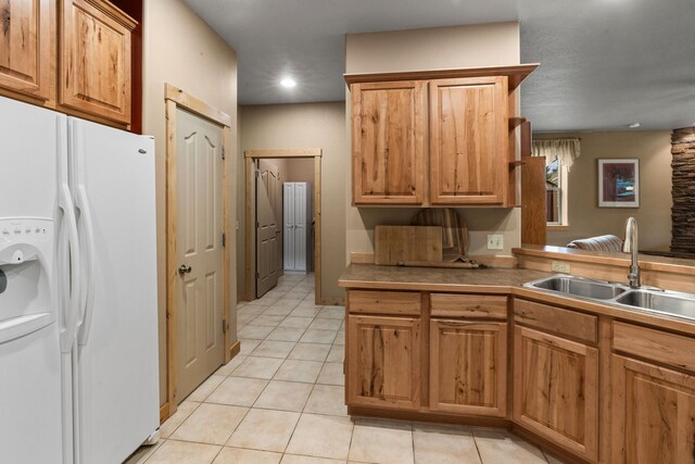 kitchen with white fridge with ice dispenser, kitchen peninsula, light tile patterned flooring, and sink